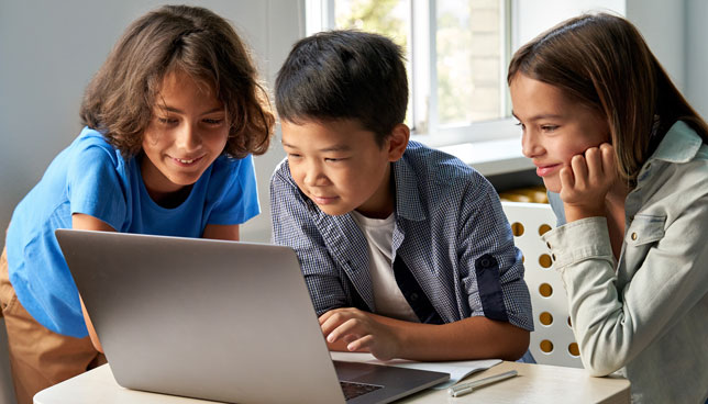 school kids using laptop computer together in classroom