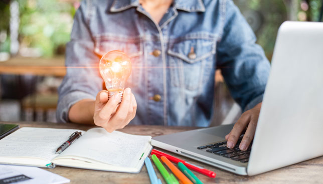 woman holding a light bulb with computer laptop and notebook