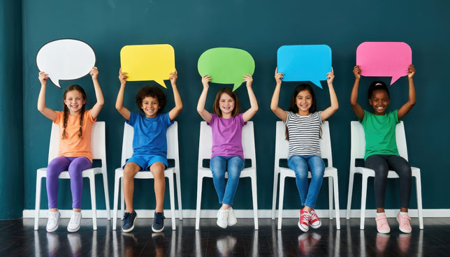 children sitting on white chairs, holding up colorful speech bubbles